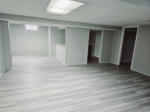 basement with a paneled ceiling and light wood-style flooring