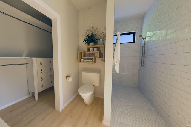 bathroom with baseboards, tiled shower, toilet, and wood finished floors