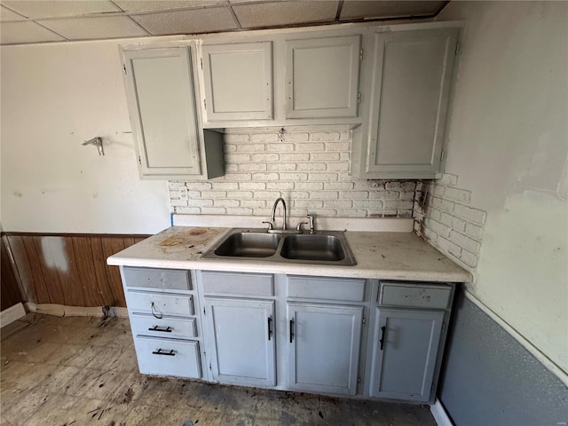 kitchen with a drop ceiling, a wainscoted wall, wood walls, a sink, and light countertops