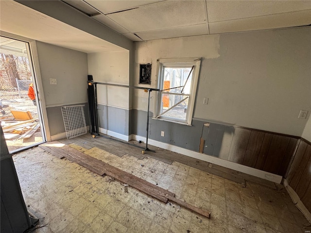 empty room with a paneled ceiling, wooden walls, and wainscoting