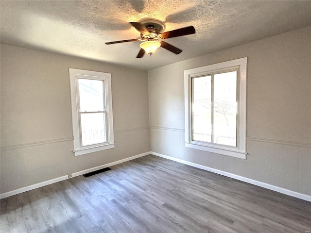 empty room with dark wood-style floors, ceiling fan, a textured ceiling, and a wainscoted wall