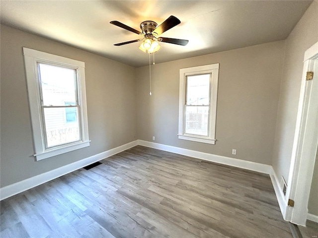 empty room featuring ceiling fan, visible vents, baseboards, and dark wood-style flooring