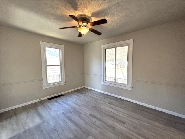 unfurnished room with plenty of natural light, visible vents, dark wood finished floors, and a textured ceiling