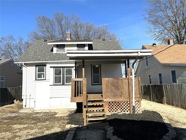 back of property featuring a porch, roof with shingles, fence, and a chimney