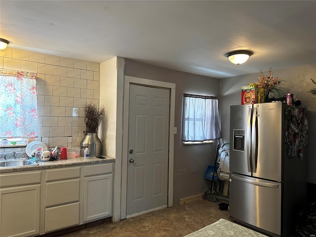 kitchen featuring stainless steel fridge, decorative backsplash, light countertops, white cabinetry, and a sink