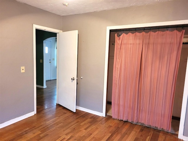 unfurnished bedroom with arched walkways, a textured ceiling, baseboards, and wood finished floors