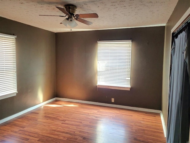 spare room with ceiling fan, a textured ceiling, baseboards, and wood finished floors