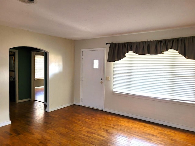 foyer entrance featuring arched walkways, wood finished floors, and baseboards