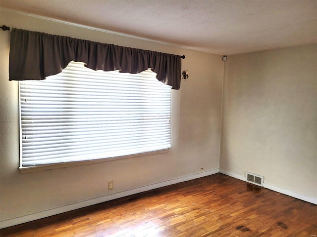 unfurnished room featuring baseboards, visible vents, and wood finished floors