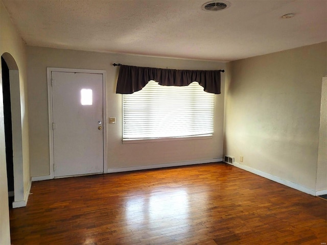 entryway with arched walkways, visible vents, a textured ceiling, and wood finished floors