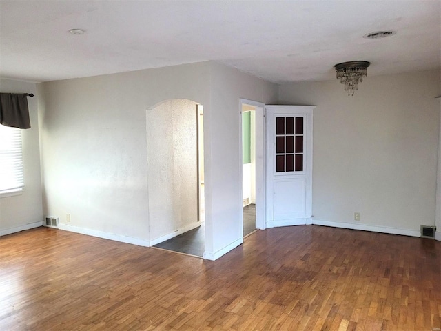 unfurnished room with arched walkways, wood finished floors, visible vents, and baseboards