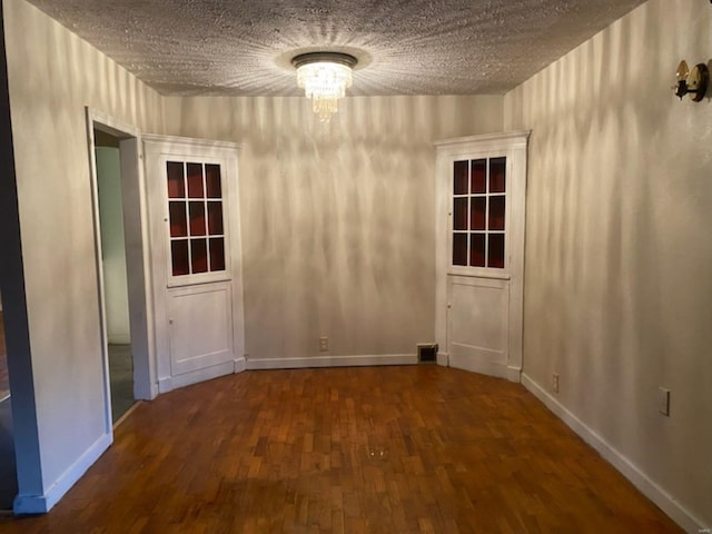 unfurnished dining area with a textured ceiling, a notable chandelier, wood finished floors, and baseboards