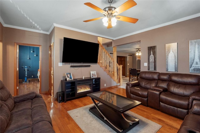 living area featuring stairs, light wood finished floors, ornamental molding, and a ceiling fan