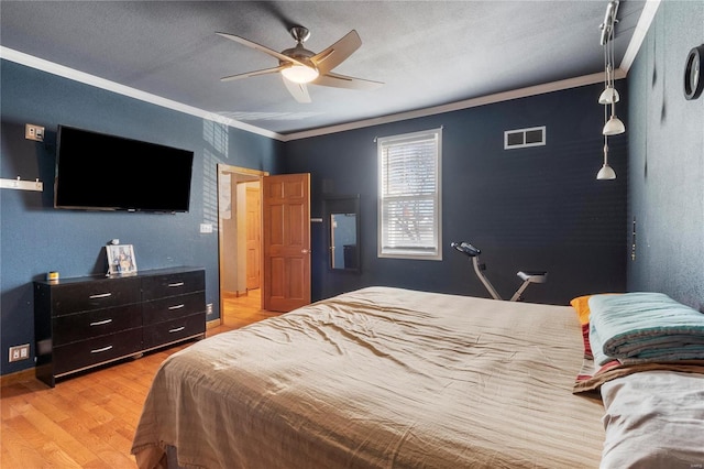 bedroom with light wood finished floors, visible vents, a ceiling fan, a textured ceiling, and crown molding