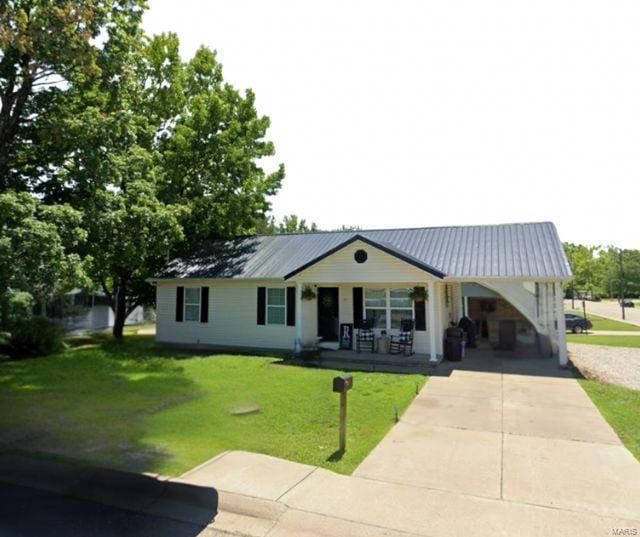 single story home with metal roof, covered porch, driveway, and a front lawn