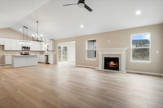 unfurnished living room featuring light wood-type flooring, vaulted ceiling, a premium fireplace, and ceiling fan with notable chandelier