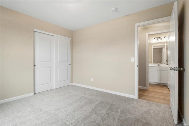 unfurnished bedroom featuring a sink, baseboards, a closet, and light colored carpet
