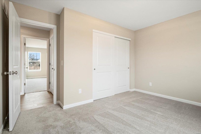 unfurnished bedroom featuring a closet, light carpet, and baseboards