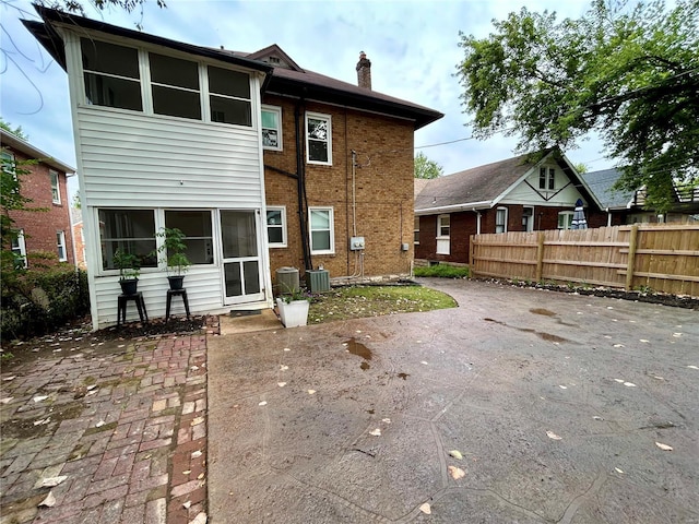 rear view of property with central AC unit, a chimney, fence, a patio area, and brick siding