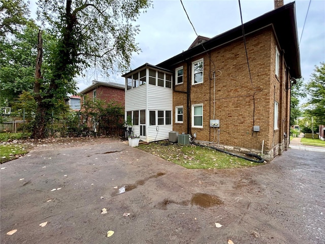 back of house featuring brick siding, a chimney, central AC unit, and a sunroom