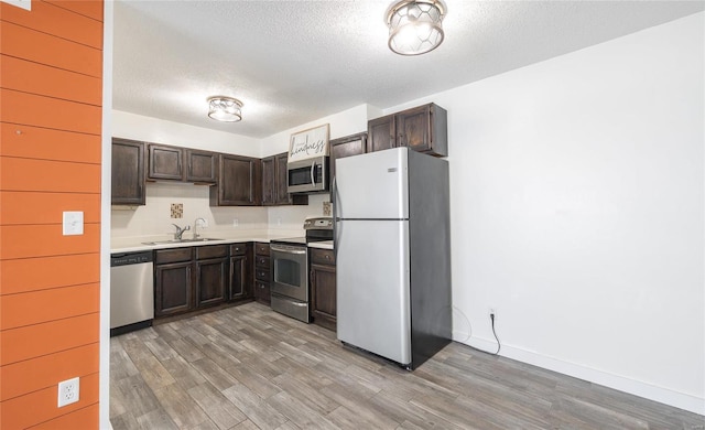 kitchen featuring dark brown cabinetry, light wood finished floors, stainless steel appliances, light countertops, and a sink