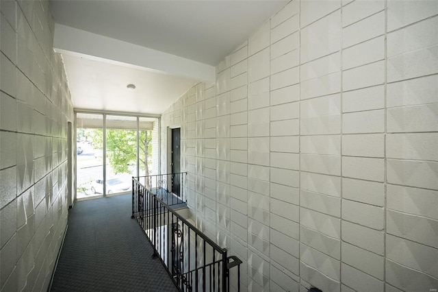 hall featuring floor to ceiling windows, vaulted ceiling with beams, tile walls, carpet flooring, and an upstairs landing