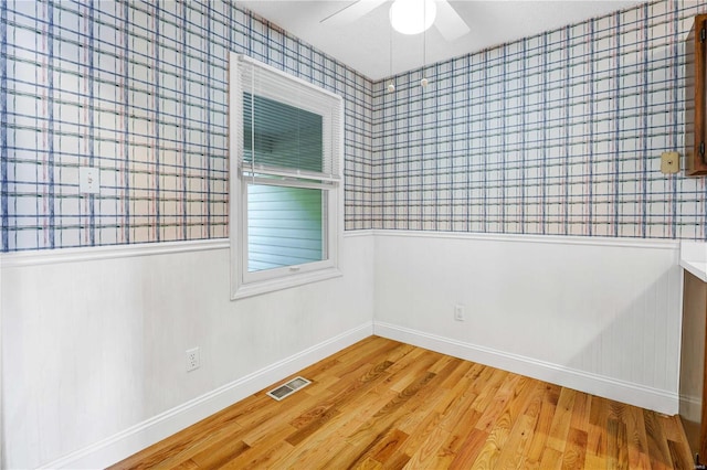 unfurnished room featuring ceiling fan, wainscoting, wood finished floors, and visible vents