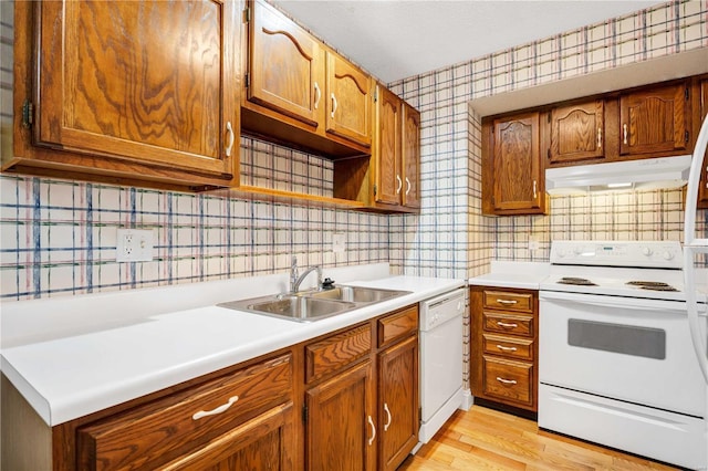 kitchen featuring brown cabinets, light countertops, a sink, white appliances, and under cabinet range hood