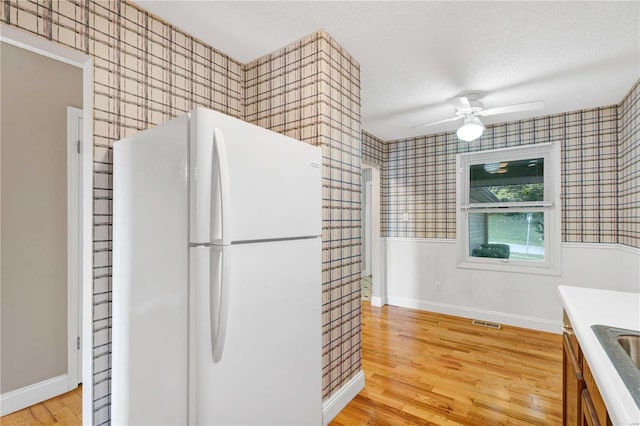 kitchen featuring a wainscoted wall, light wood finished floors, freestanding refrigerator, a textured ceiling, and wallpapered walls