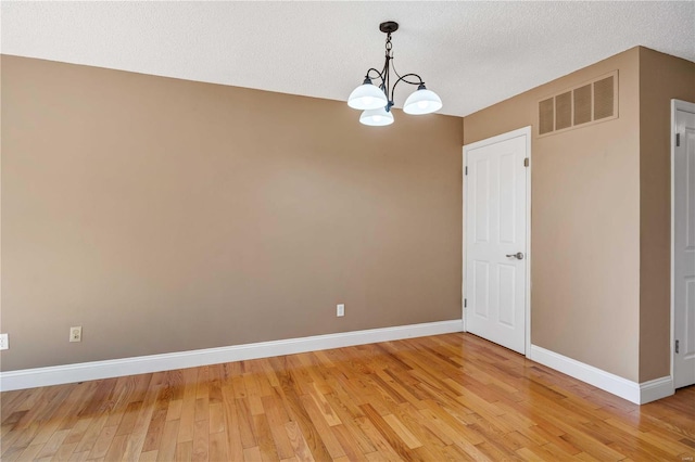 empty room featuring baseboards, visible vents, wood-type flooring, and a textured ceiling