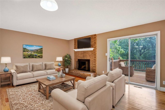 living area featuring light wood-style flooring, a fireplace, visible vents, and a textured ceiling