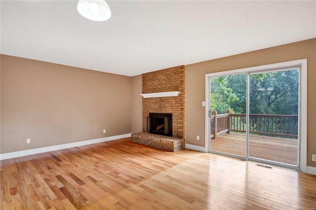 unfurnished living room featuring light wood finished floors, baseboards, a brick fireplace, and visible vents