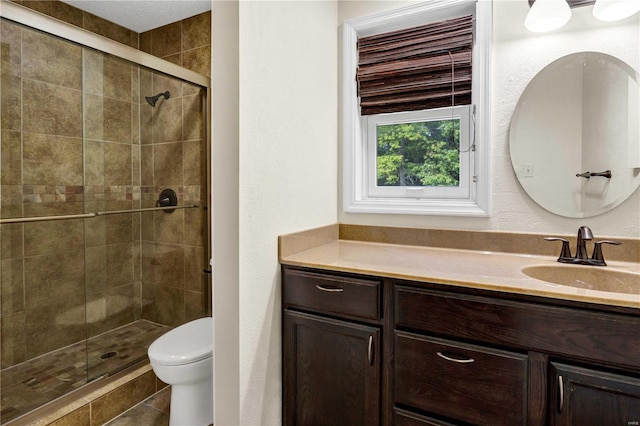 bathroom featuring toilet, a textured wall, a shower stall, and vanity