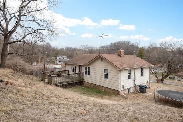 rear view of property featuring a shingled roof, a chimney, a trampoline, a deck, and cooling unit