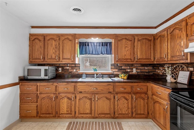 kitchen featuring dark countertops, stainless steel microwave, brown cabinets, black range with electric stovetop, and a sink