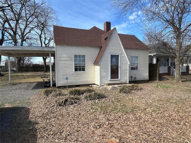 rear view of property with driveway, a shingled roof, and a chimney