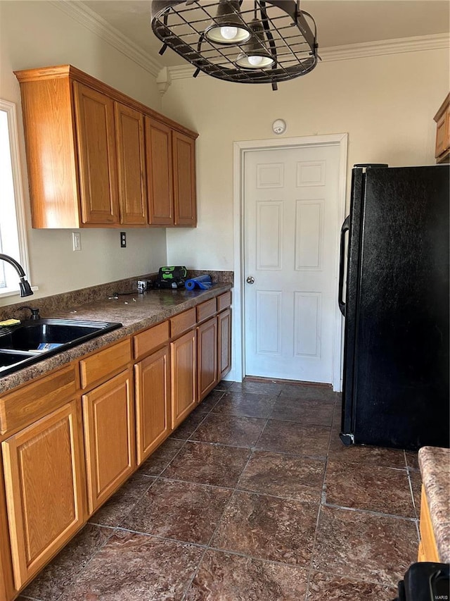 kitchen featuring brown cabinets, dark countertops, ornamental molding, freestanding refrigerator, and a sink