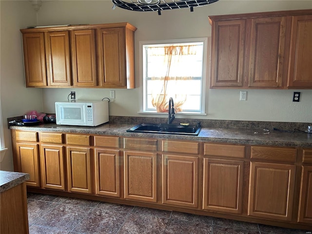 kitchen with dark countertops, brown cabinets, a sink, and white microwave