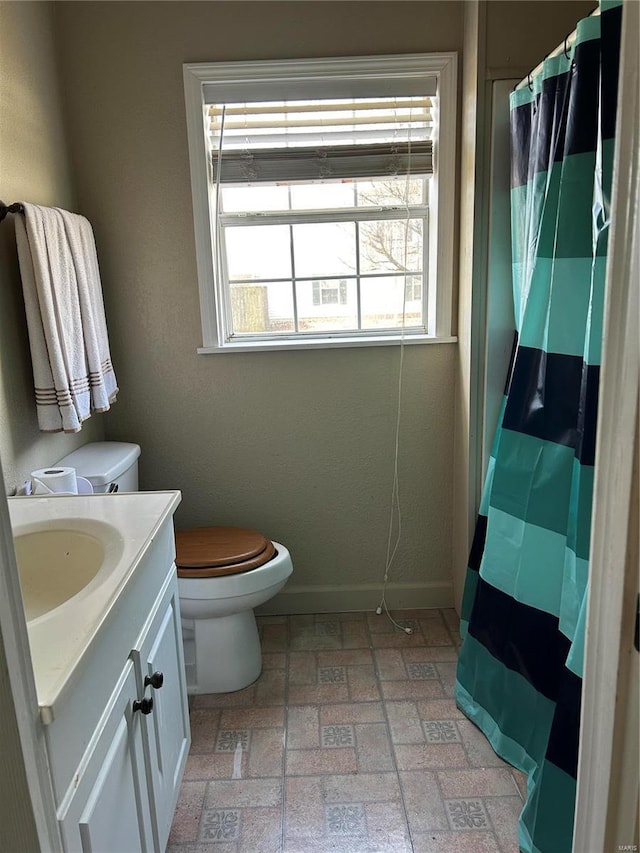 full bath featuring curtained shower, brick floor, toilet, vanity, and baseboards