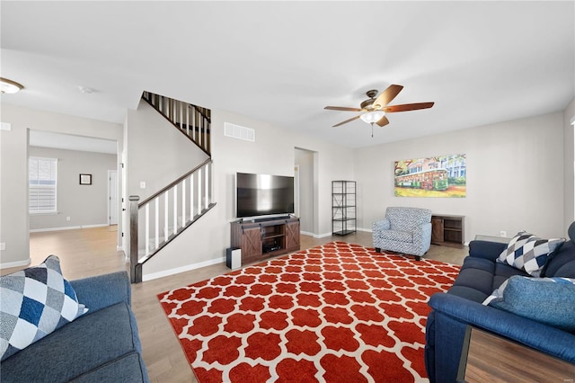 living area featuring baseboards, visible vents, ceiling fan, wood finished floors, and stairs