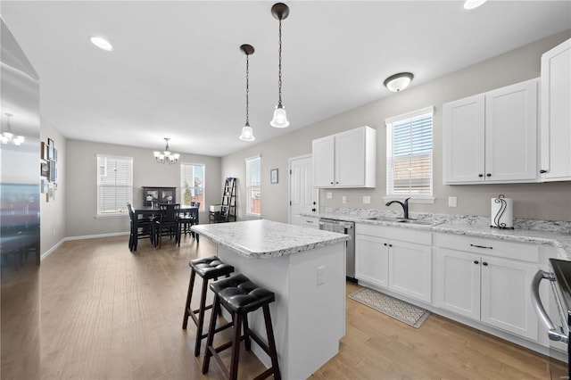 kitchen with a kitchen island, a sink, an inviting chandelier, light wood-style floors, and stainless steel dishwasher