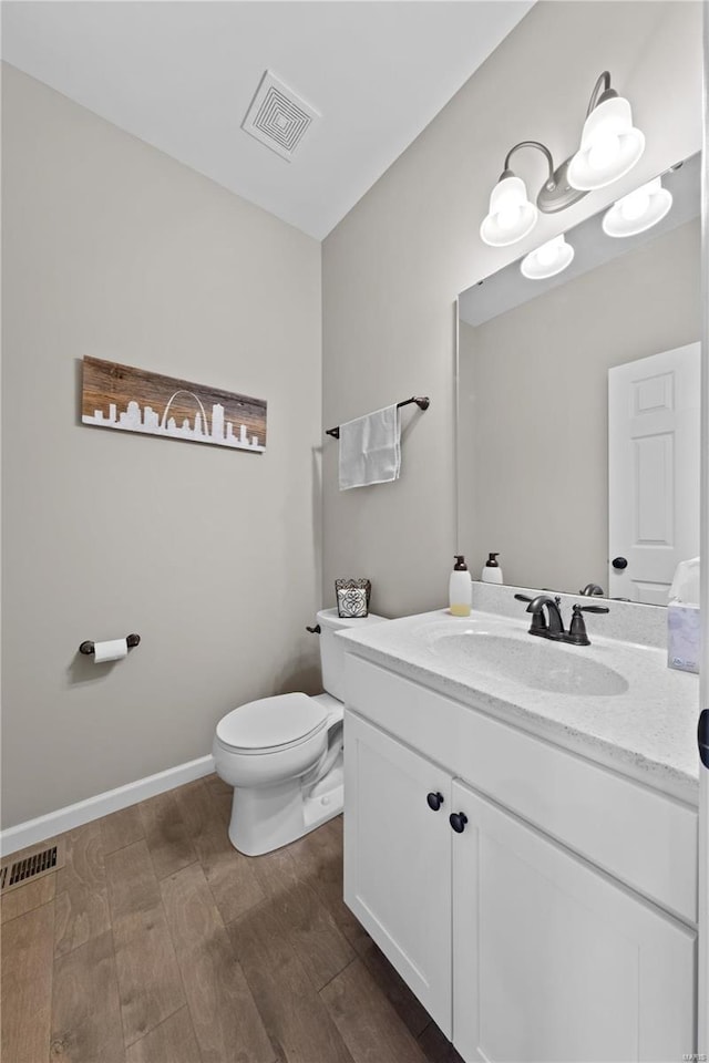 bathroom with toilet, wood finished floors, vanity, visible vents, and baseboards