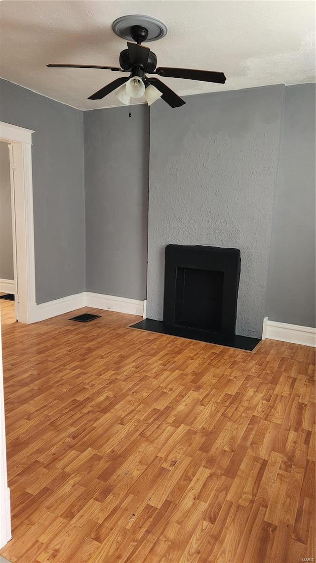 unfurnished living room with visible vents, a fireplace with flush hearth, light wood-style floors, a textured ceiling, and baseboards