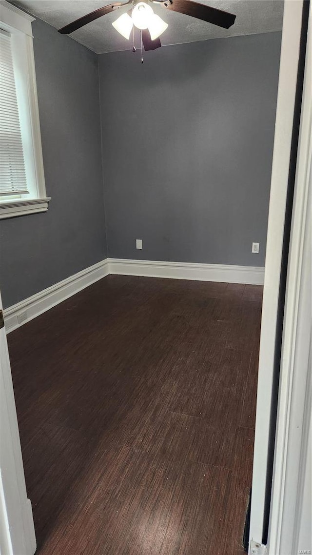 empty room featuring a textured ceiling, dark wood-style flooring, a ceiling fan, and baseboards