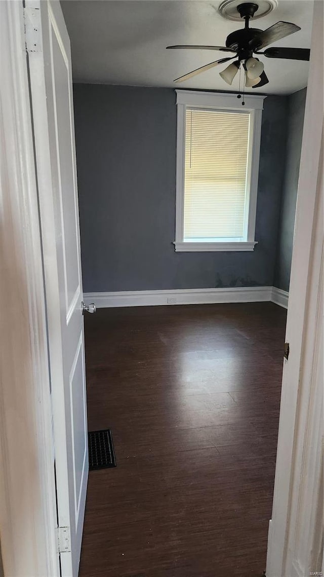 empty room with a ceiling fan, visible vents, baseboards, and wood finished floors