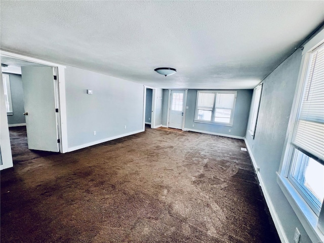 empty room with dark carpet, a textured ceiling, and baseboards