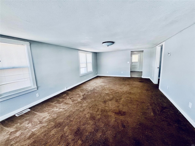 spare room featuring dark colored carpet, visible vents, a textured ceiling, and baseboards