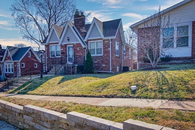 tudor home featuring brick siding, central AC, a chimney, and a front lawn