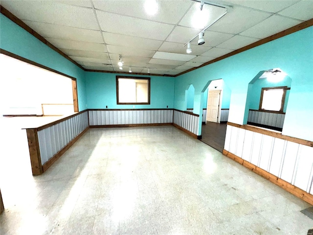 empty room featuring arched walkways, ornamental molding, a drop ceiling, and tile patterned floors