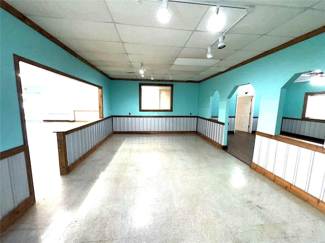 unfurnished room with a paneled ceiling, a wainscoted wall, arched walkways, and ornamental molding